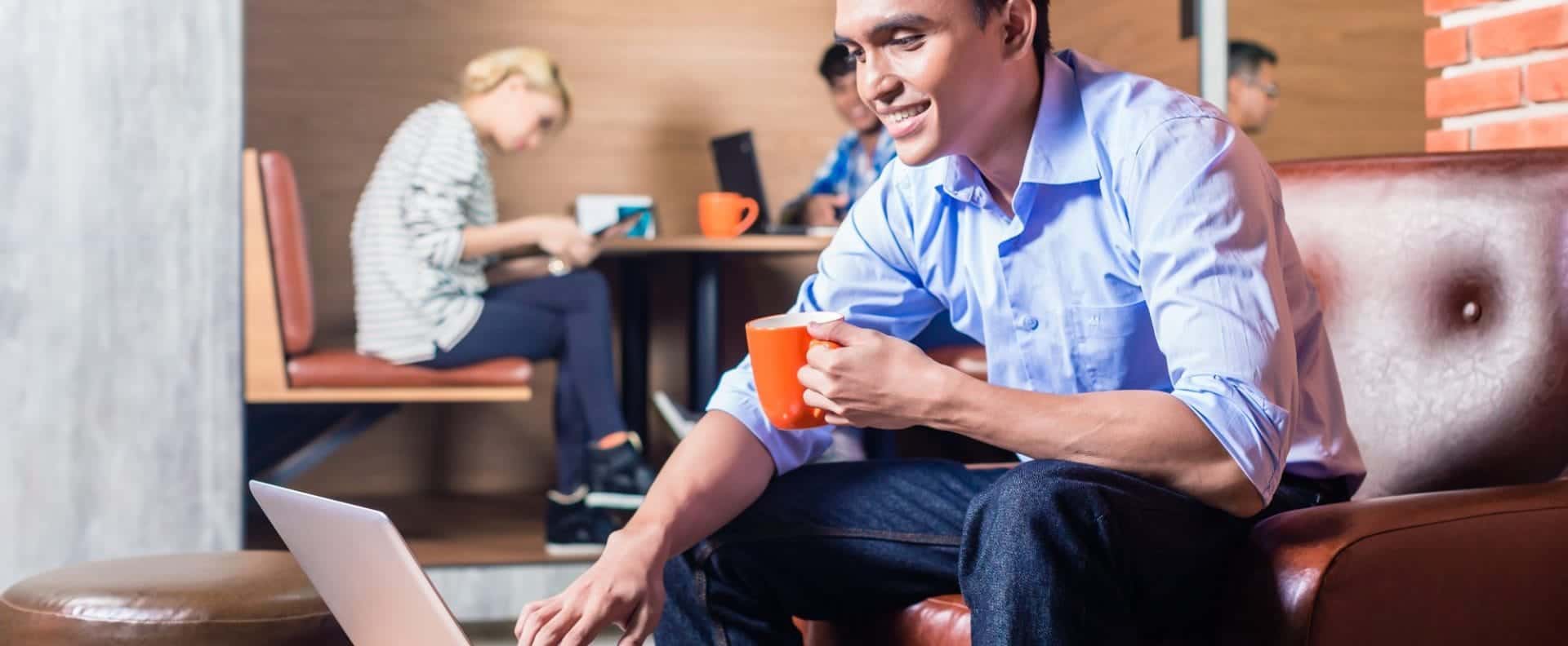 Man working on a leather couch on his laptop drinking coffee